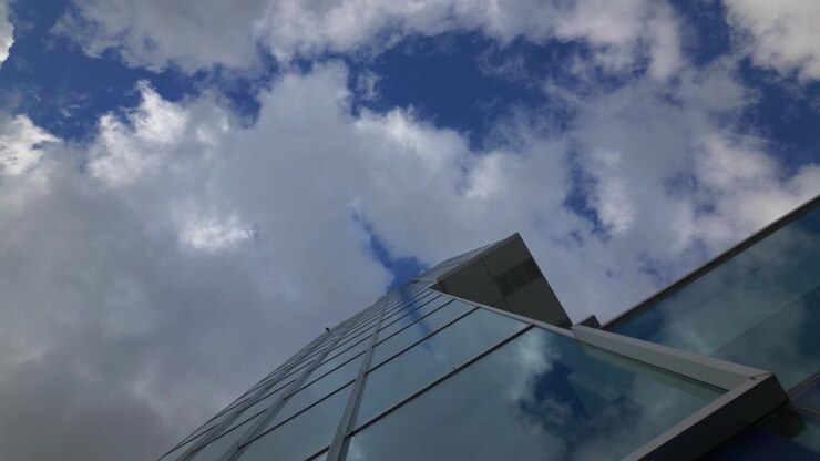 Una vista de ángulo bajo hacia una torre de cristal en el Puerto Viejo de Montreal, con nubes reflejadas en la cuadrícula de sus ventanas y un techo proyectado sobre ella