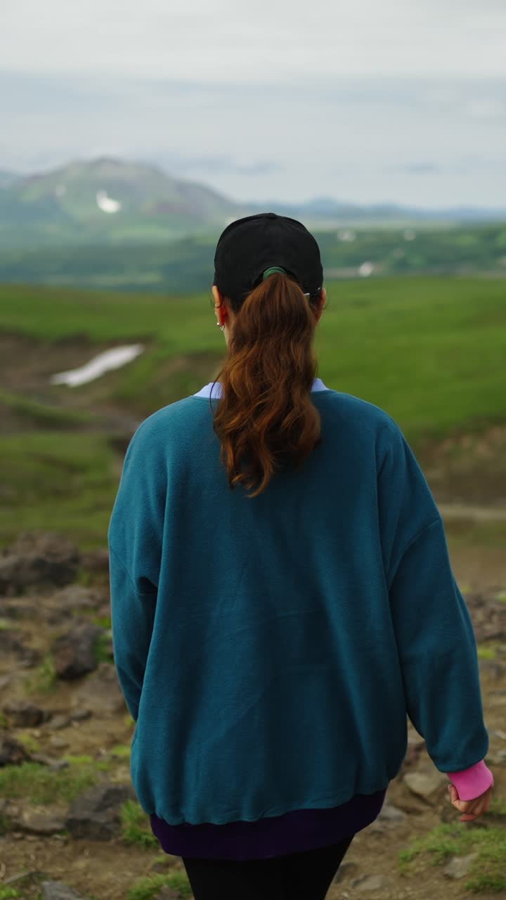 Rear View of Woman Walking Through Green Mountain Landscape
