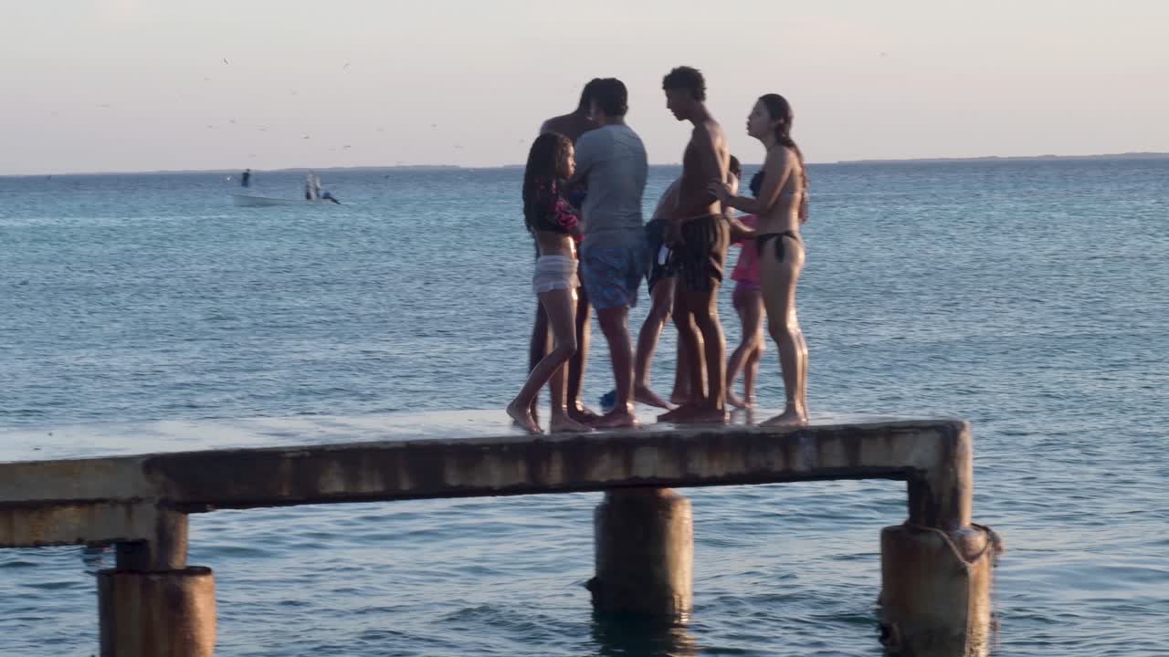 Group of young friends having fun at sunset beach on fishing pier. Summer vacations concept