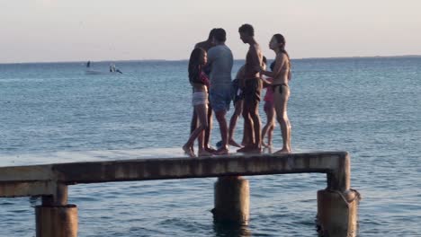 group of young friends having fun at sunset beach on fishing pier. summer vacations concept
