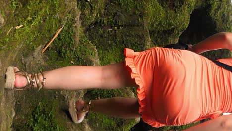 vertical shot of young tourist in orange dress running along the rocks to the top during her summer trip through bali indonesia