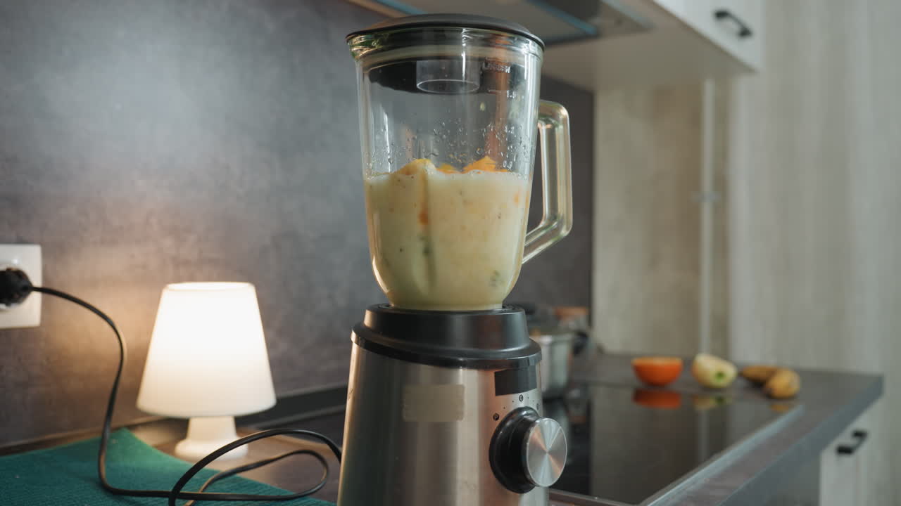 Kremet prenatal smoothie blandes i blender med skummende bevegelse og tykk tekstur, varm benkeplate-lampeatmosfære, gulgrønn farge, klar til servering for næring, gledelig morsritual i hjemmet.