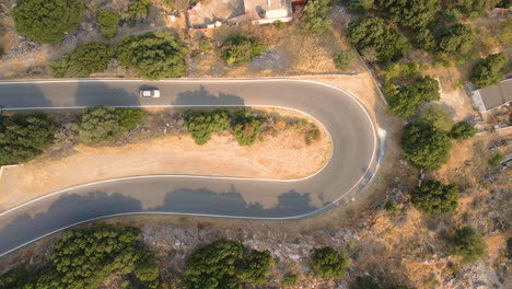 top view of white car driving slowly through a curved road in crete island, greece