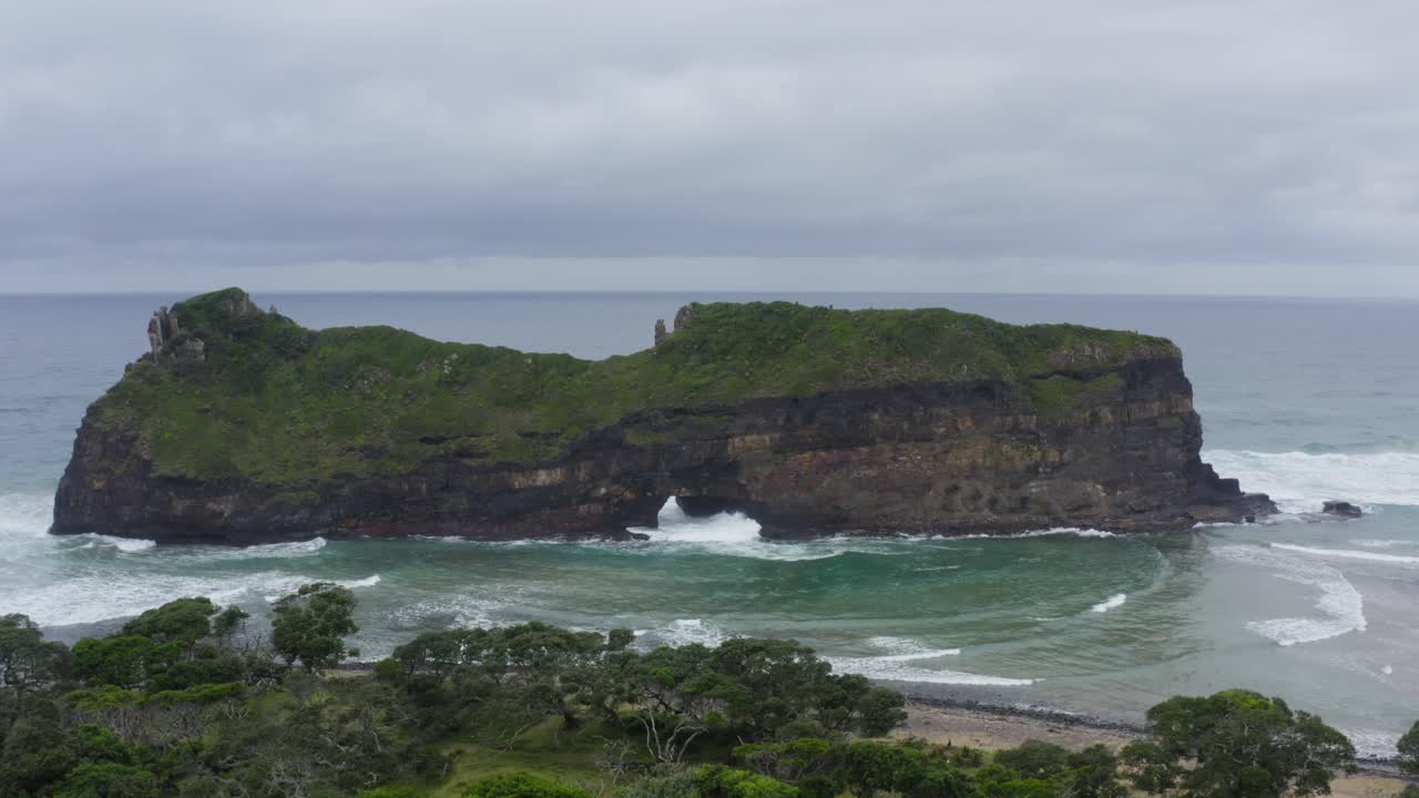 drone volando hacia el agujero en la formación rocosa de la pared en el océano índico con hierba verde, transkei sudáfrica