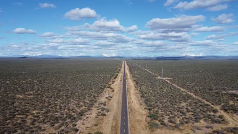 a long straight road cutting through the vast desert of baja california sur, under a blue sky with clouds, aerial view