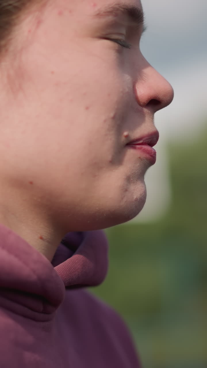 primer plano de una mujer corriendo con una sudadera roja con la capucha con el viento arruinando su cabello, el fondo borroso con vegetación y una cancha deportiva visible, capturando su movimiento enfocado y enérgico