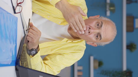 Vertical-video-of-Home-office-worker-old-man-looking-at-camera-confused.