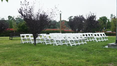 sillas plegables blancas dispuestas en filas sobre un césped verde preparado para una ceremonia de boda en el jardín