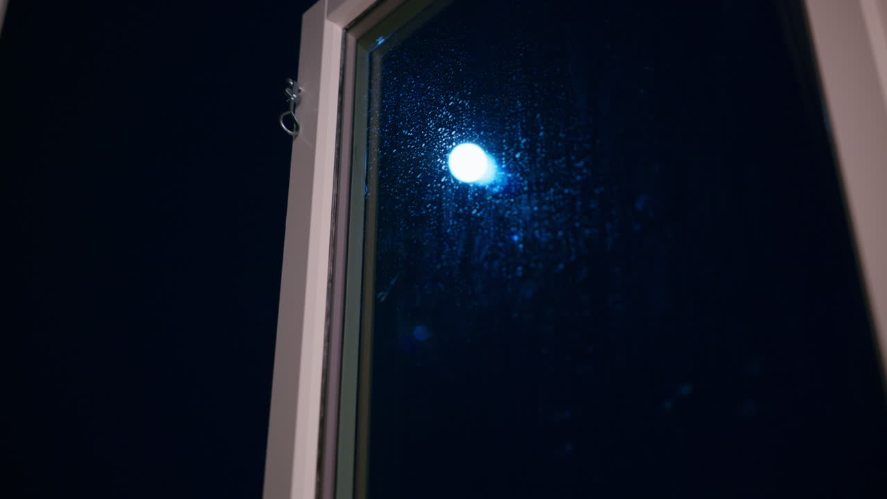 La luna splende luminosa in una notte fredda e buia e mostra l'acqua che gocciola sulla finestra.