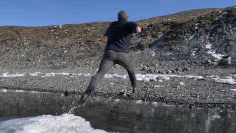 young male traveler jumping off a ice floe in beautiful glacial lagoon in iceland in slow motion