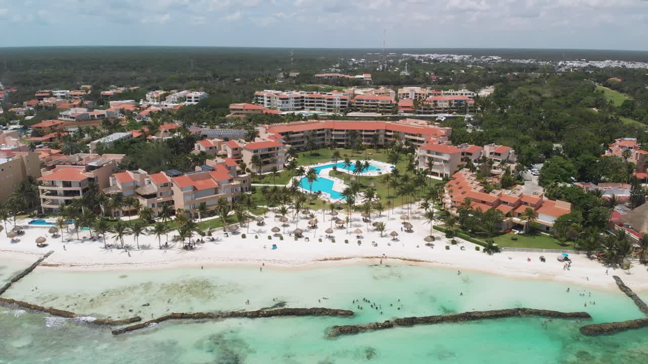 Tilt aerial shot revealing turquoise sea transitioning to tropical beachfront resorts and dense greenery in Puerto Aventuras