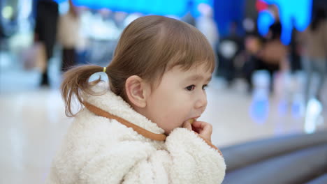 Vista-Lateral-De-Una-Niña-Pequeña-De-3-Años-Sentada-Comiendo-Pan-Dentro-De-Un-Centro-Comercial