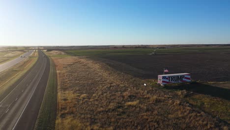 aerial drone video donald trump 2024 presidential election campaign sign painted on a large truck or trailer with cars driving on highway in rural farm land with oil rig in the middle of nowhere