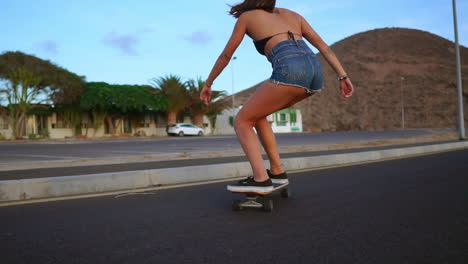 Con-El-Telón-De-Fondo-De-Montañas-Y-Un-Hermoso-Cielo,-Una-Mujer-Practica-Skate-En-Cámara-Lenta-En-Una-Carretera-Al-Atardecer.-Ella-Usa-Pantalones-Cortos