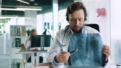 close-up view of senior male doctor with headphones sitting at desk speaking at camera and explaining coronavirus lung disease in hospital office