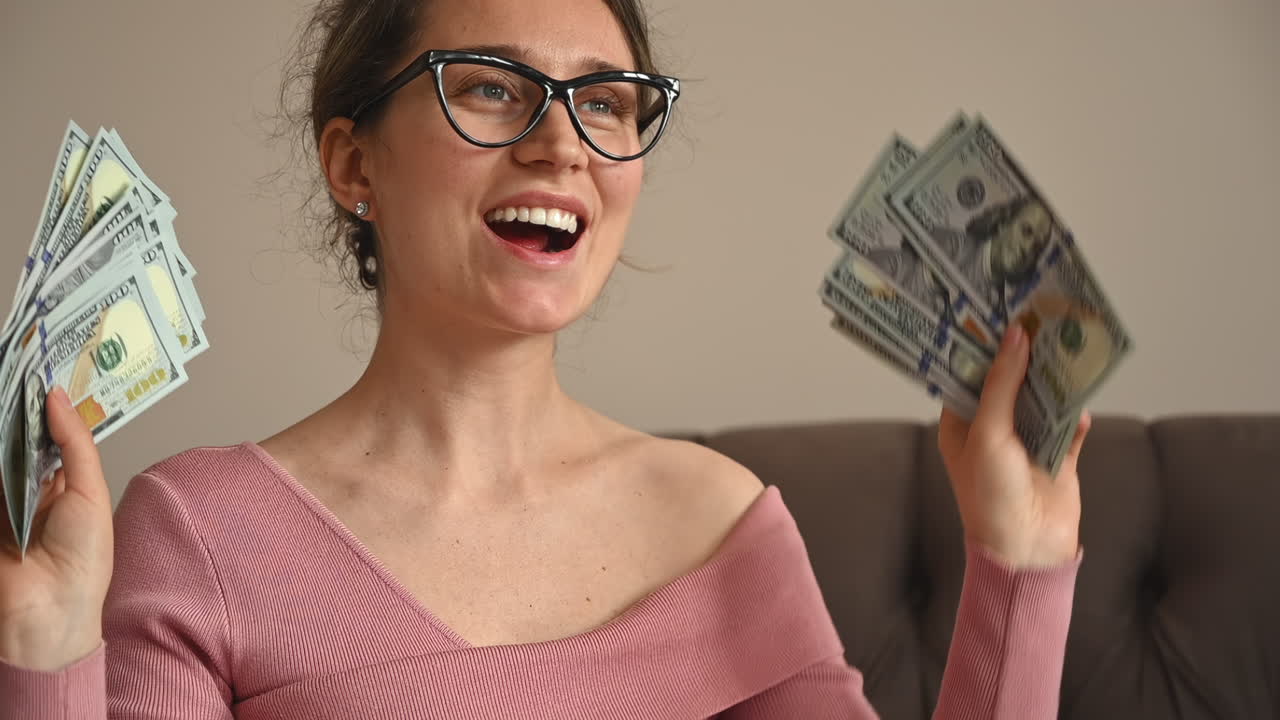Smiling woman admiring a large fan of one hundred dollar bills in her hands