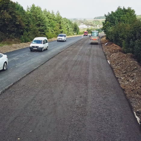 vibratory roller compresses fresh asphalt on one side of the road on the background of the movement of cars on the other side of the road. modern equipment for road construction works. aerial view.