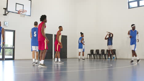 multiracial male basketball players playing basketball, coach pausing game and team huddling in gym