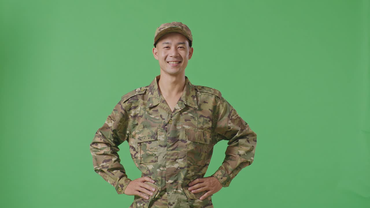 Asian Man Soldier Standing With Arms Akimbo Looking At Camera And Smiling In The Green Screen Background Studio