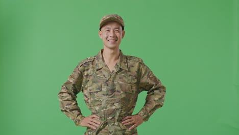 Asian Man Soldier Standing With Arms Akimbo Looking At Camera And Smiling In The Green Screen Background Studio