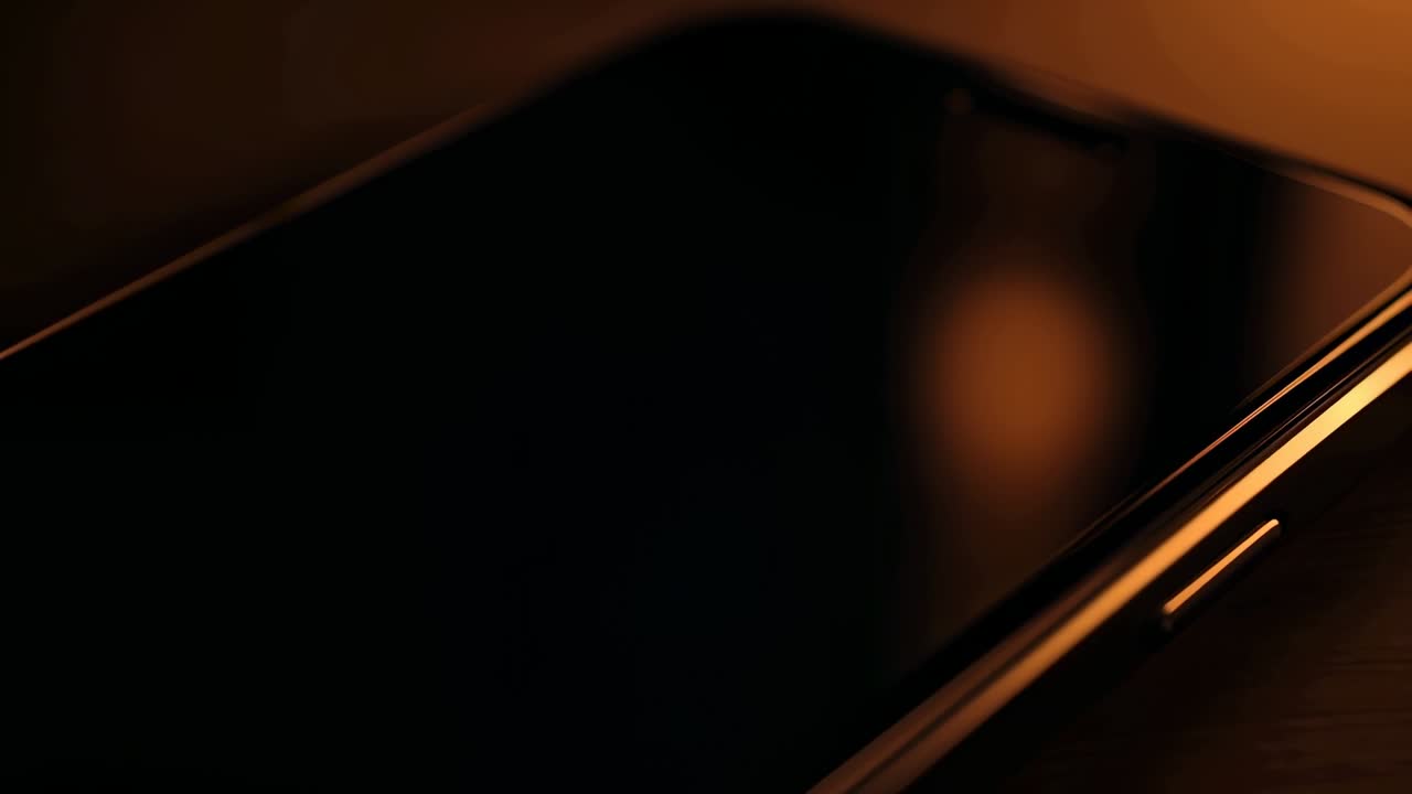 La telecamera si avvicina, un telefono appoggiato mostra lo schermo lucido e il bordo metallico con i pulsanti laterali, per una pubblicità tecnologica.