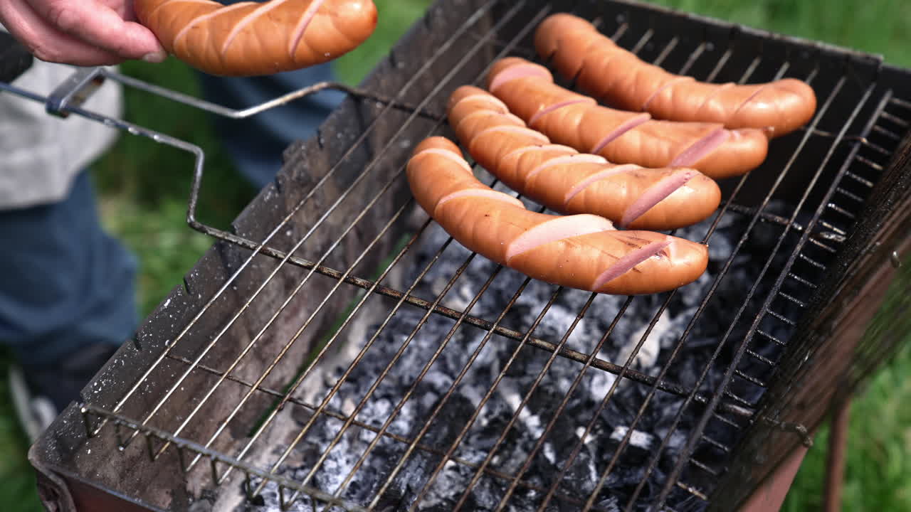Preparation for grilling sausages. Sausages with incisions on the grill. Process of preparing tasty hot dogs. Barbeque outdoors. Time for picnic.