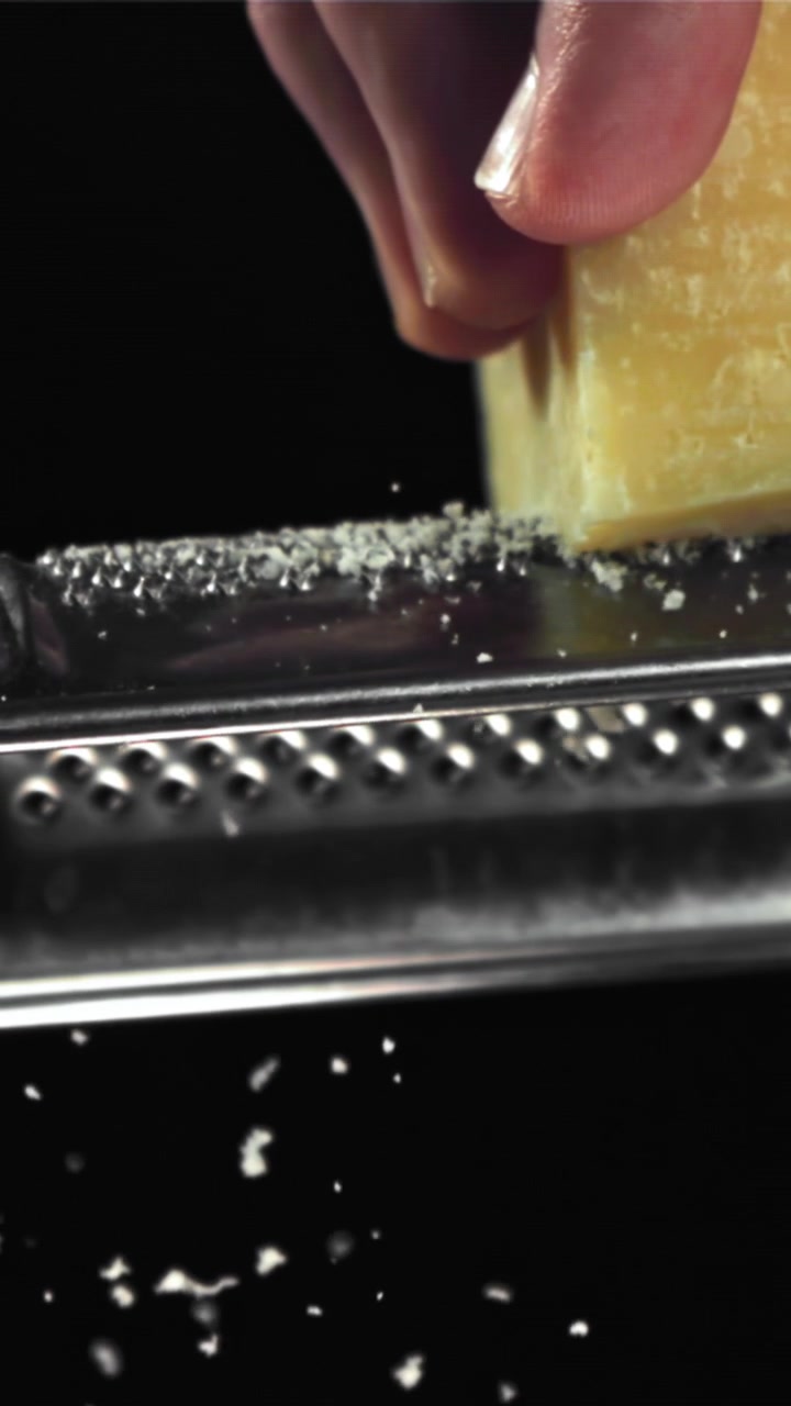Primo piano di una mano che grattugia Parmigiano Reggiano al rallentatore