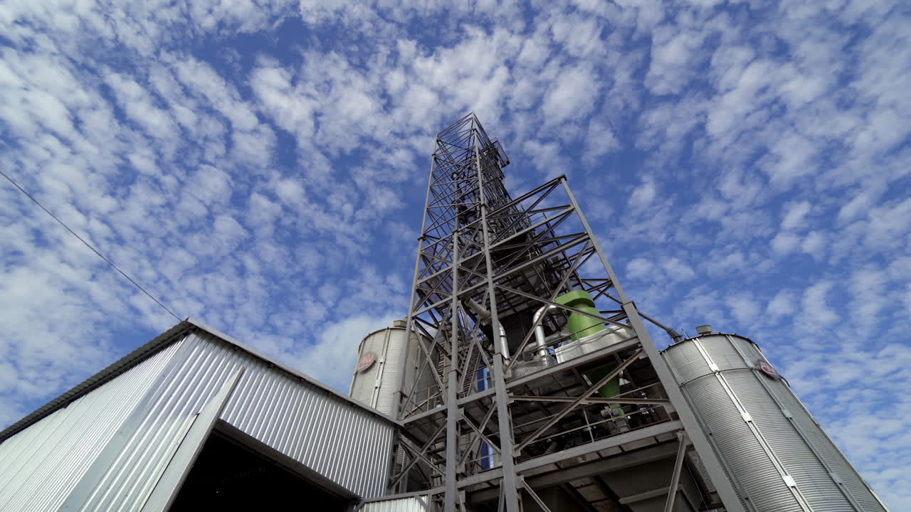 Metal granary complex under beautiful sky. Grain elevators with storage tanks for agricultural products. Close-up. View from below.