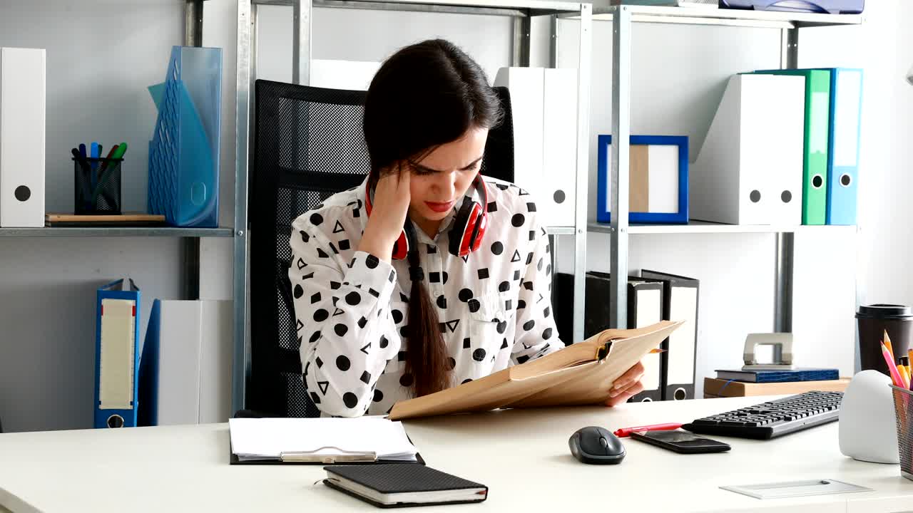 mujer con auriculares rojos en los hombros escribiendo con lápiz en papel en una oficina moderna