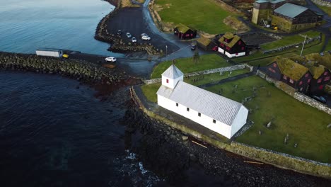 toma de la órbita de la puesta de sol de drones de la iglesia en el pueblo de kirkjubour con vista al mar en las islas feroe en un día soleado de verano