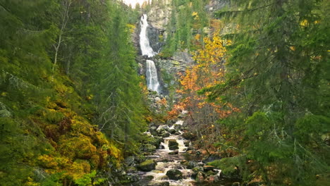 autumn forest with scenic waterfall in sweden - aerial pullback