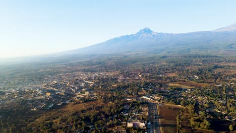 Amanecer:-Paisaje-De-Kenia-Con-Un-Pueblo,-Kilimanjaro-Y-El-Parque-Nacional-De-Amboseli---Seguimiento,-Vista-Aérea-De-Drones