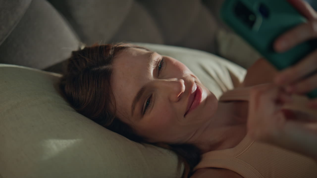 Girl smartphone lying bed pillows waking up early morning close up. Sleepy woman