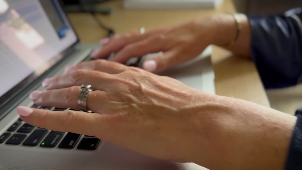 Closeup of mature woman with manicured hands in a nightdress using a laptop