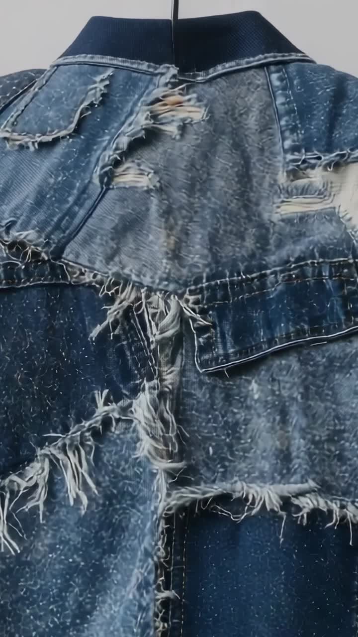 Vertical video: Panning camera revealing worn denim jacket on black hanger in studio, showing patch