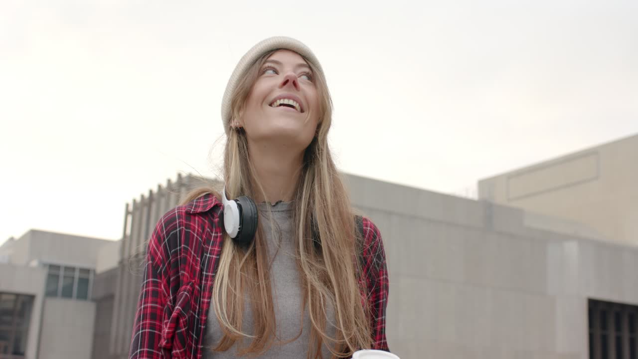 Female in early twenties holding coffee cup on rooftop terrace spotting movement above and smiling
