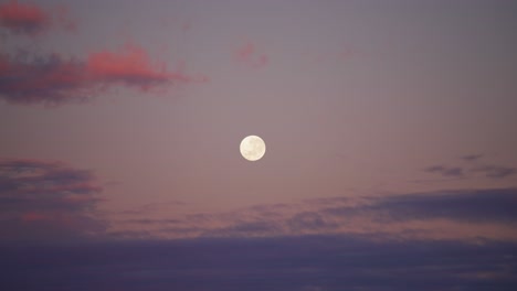 full moon in the morning or evening sky surrounded by colourful clouds