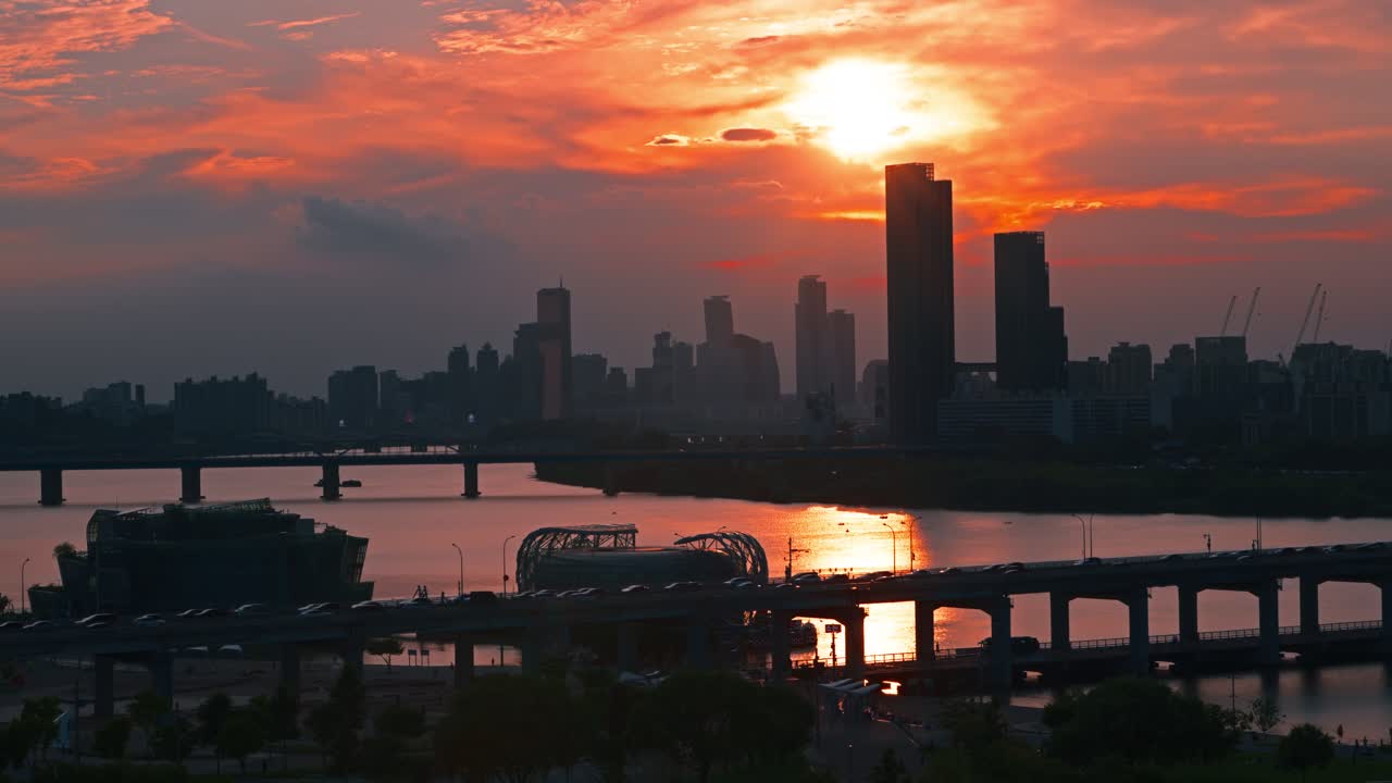 Bright orange sunset fills Seoul skyline as skyscrapers, Han River and traffic on Banpo Bridge appear in striking silhouette from aerial perspective