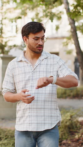 serious dissatisfied young indian man standing outdoors looking for someone waiting on city street