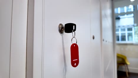 close-up view of a key inserted in a keyhole with a red key tag hanging, against a white background