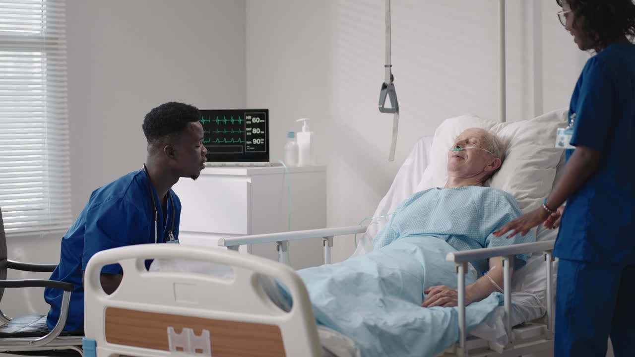 equipo de jóvenes médicos africanos consultando a un paciente infectado con covid-19 en la cama del hospital. hombre enfermo acostado en la cama del hospital y hablando con el cirujano con ropa y máscara protectora. médico examinando a un paciente anciano