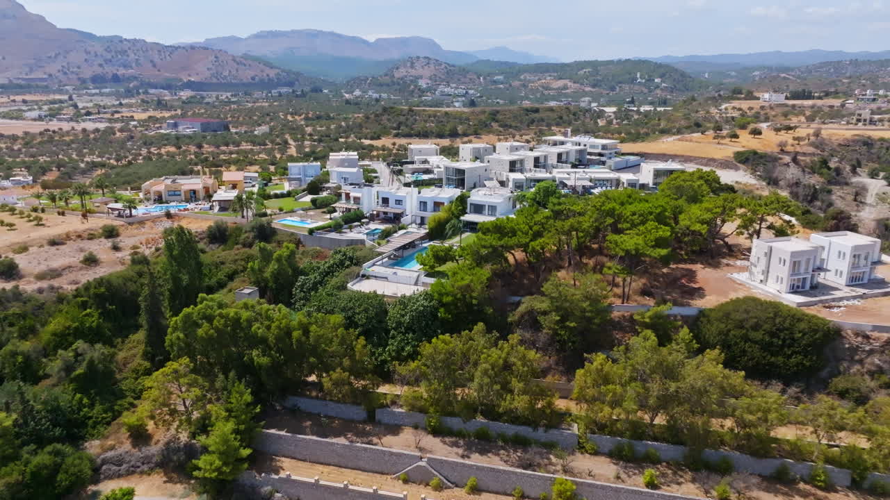 Aerial view approaching holiday homes on top of a hill, sunny day in Greece