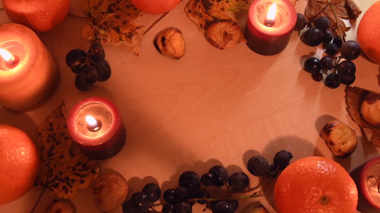Vista dall'alto di uno sfondo autunnale con foglie, mandarino, castagne, candele e uva.