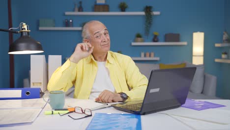 home office worker old man scratches his ears looking at camera.