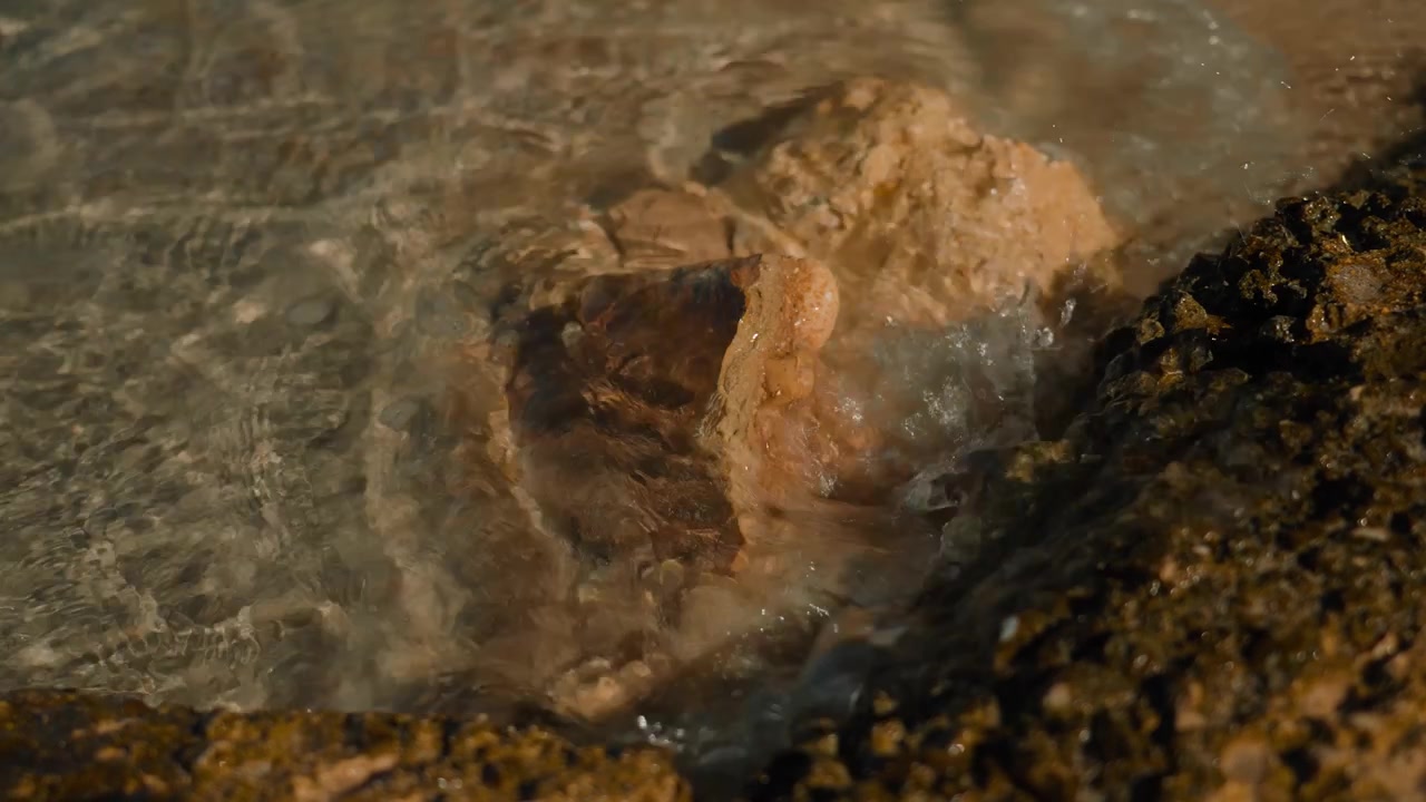 Chiare onde del Mar Mediterraneo si infrangono dolcemente su formazioni rocciose vulcaniche su una spiaggia siciliana