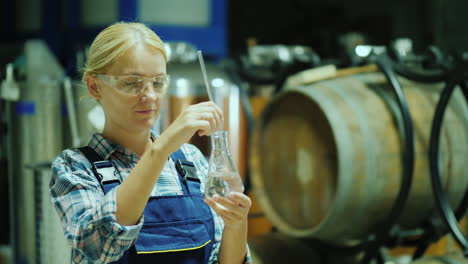 Female-Researcher-Working-With-Product-Samples-In-A-Flask-Against-The-Background-Of-Wooden-Barrels-O