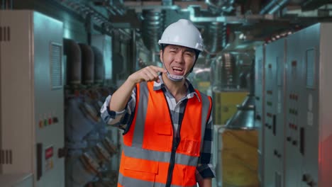 angry asian male engineer with safety helmet shouting at someone while standing in engine control room, work of electrical generators