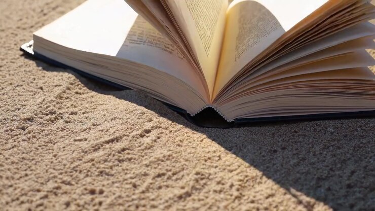 Pagine di un libro aperto che svolazzano sulla sabbia alla luce del sole