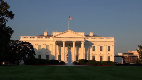 the white house in washington d.c. with an american flag and fountain on a clear day