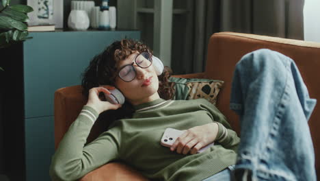 relaxed girl chilling on couch at home, listening to music on headphones